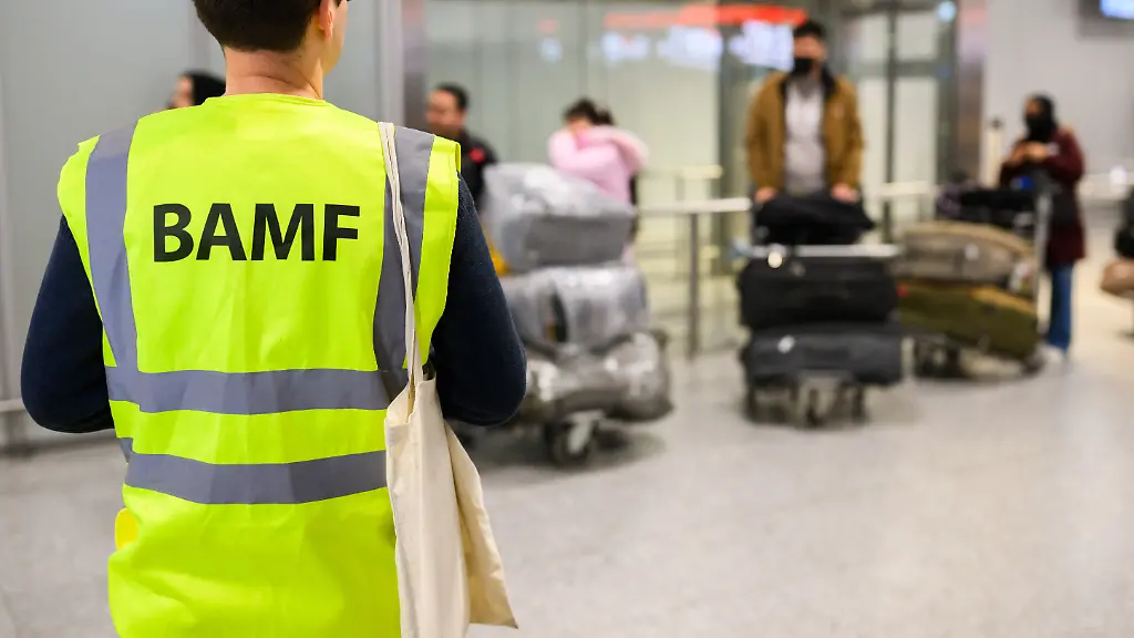 Ein-Mitarbeiter-vom-BAMF-Bundesamt-fuer-Migration-und-Fluechtlinge-steht-im-Flughafen-Hannover-vor-Afghaninnen-und-Afghanen-aus-den-Bundesaufnahmeprogrammen