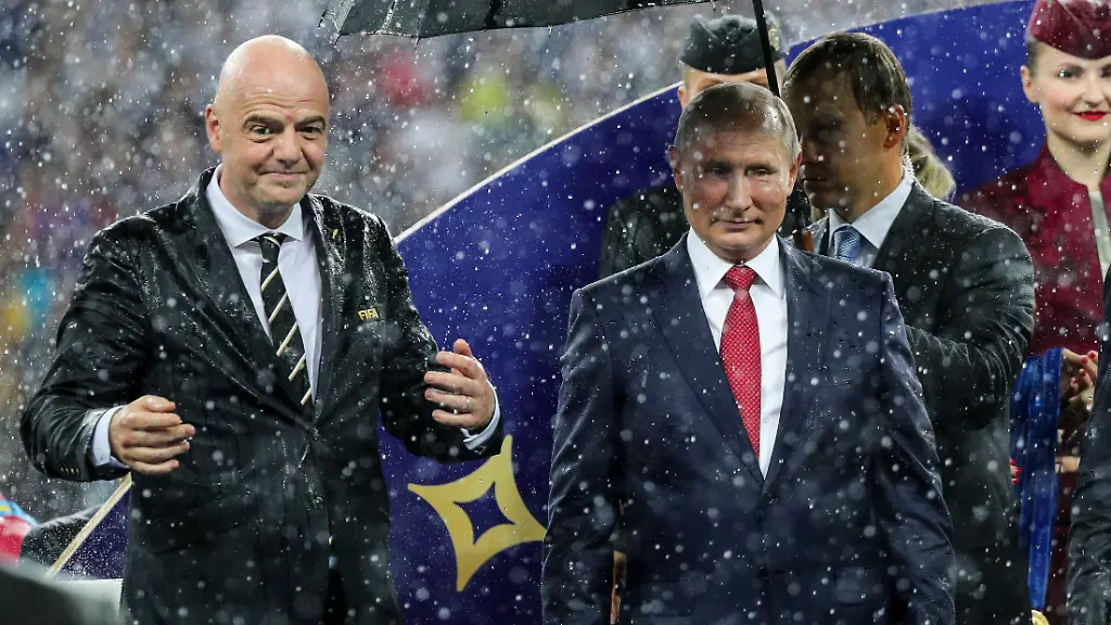 ARCHIV-15-07-2018-Russland-Moskau-15-07-2018-Russland-Moskau-Fussball-WM-Frankreich-Kroatien-FIFA-Praesident-Gianni-Infantino-l-r-Wladimir-Putin-Praesident-von-Russland-und-Emmanuel-Macron-Praesident-von-Frankreich-stehen-nach-dem-Spiel-auf-einem-Podest-im-stroemenden-Regen