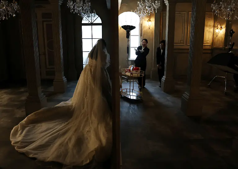 Wedding-planners-Sayaka-Ogasawara-and-Naoki-Ogasawara-a-married-couple-who-specialize-in-ceremonial-weddings-with-virtual-and-two-dimensional-characters-talk-to-Yurina-Noguchi-32-after-placing-her-smartphone-displaying-an-AI-generated-image-of-Klaus-her-AI-partner-next-to-her-during-a-photo-session-at-the-Magritte-wedding-venue-in-Okayama-Japan-October-27-2025-REUTERS-Kim-Kyung-Hoon-SEARCH-JAPAN-KYUNG-HOON-AI-WEDDING-FOR-THIS-STORY-SEARCH-WIDER-IMAGE-FOR-ALL-STORIES