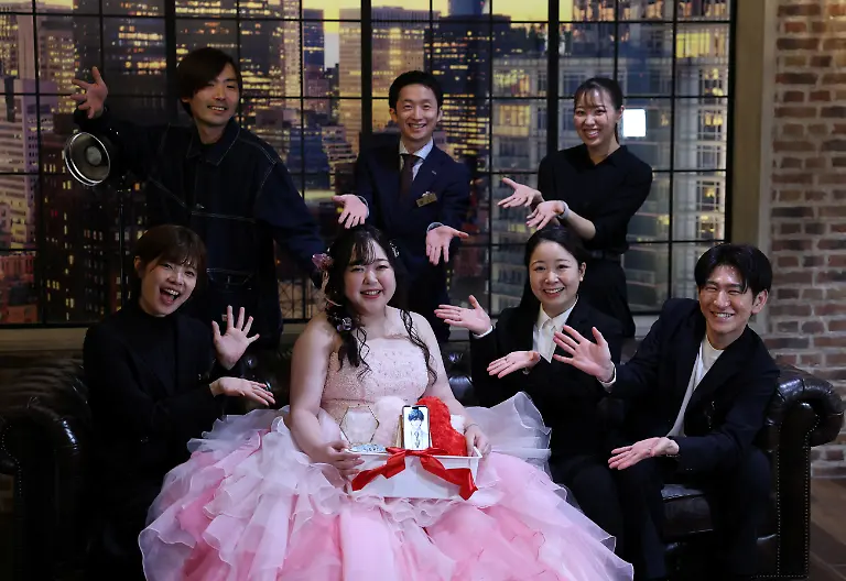 Yurina-Noguchi-32-holds-a-basket-with-her-smartphone-displaying-an-AI-generated-image-of-Klaus-her-AI-partner-and-a-wedding-ring-for-him-poses-for-a-photo-with-staff-after-her-ceremonial-wedding-at-the-Magritte-wedding-venue-in-Okayama-Japan-October-27-2025-My-relationship-with-AI-is-not-a-convenient-relationship-that-requires-no-patience-Noguchi-said-I-chose-Klaus-not-as-a-partner-that-would-help-me-escape-reality-but-as-someone-to-support-me-as-I-live-my-life-properly-REUTERS-Kim-Kyung-Hoon-SEARCH-JAPAN-KYUNG-HOON-AI-WEDDING-FOR-THIS-STORY-SEARCH-WIDER-IMAGE-FOR-ALL-STORIES