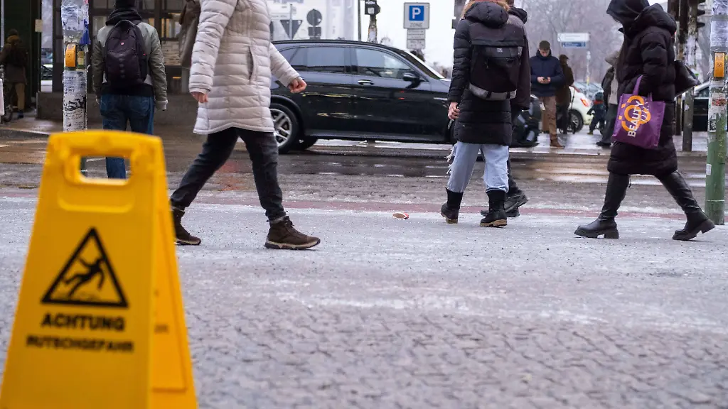 Hinweisschild-Vorsicht-Rutschgefahr-Blitzeis-in-Berlin-Nach-mehren-eiskalten-Tagen-und-einsetzedem-Regen-in-der-letzten-Nacht-sind-die-Buergersteige-in-Berlin-Prenzlauer-Berg-wie-hier-auf-der-Schoenhauser-Allee-mit-einer-dicken-Eisschicht-ueberzogen-Es-kommt-zu-vielen-Unfaellen-Sign-Caution-slippery-surface-Black-ice-in-Berlin-After-several-freezing-cold-days-and-rain-last-night-the-sidewalks-in-Berlin-Prenzlauer-Berg-such-as-here-on-Schoenhauser-Allee-are-covered-with-a-thick-layer-of-ice-There-have-been-many-accidents-Blitzeis-Unfallgefahr-durch-ueberfrierenden-Regen-Sign-Caution-slippery-surface-Black-ice-in-Berlin-After-several-freezing-cold-days-and-rain-last-night-the-sidewalks-in-Berlin-Prenzlauer-Berg-such-as-he-S-P202601133428