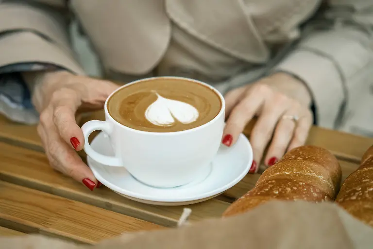 Hands-holding-a-cup-of-coffee-and-baguettes-on-a-wooden-table