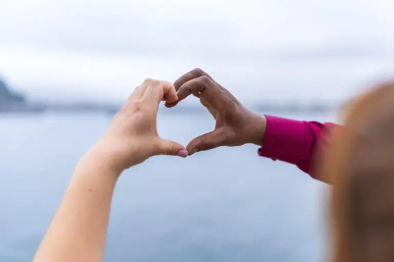 Braut-und-Braeutigam-bilden-mit-ihren-Haenden-eine-Herzform-vor-einer-atemberaubenden-Meereslandschaft-und-feiern-so-die-Liebe-und-Einheit-an-ihrem-Hochzeitstag