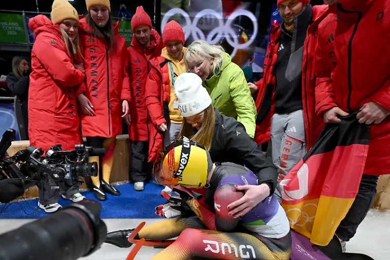 Olympia-Olympische-Winterspiele-Mailand-Cortina-2026-Rodeln-Einsitzer-Frauen-Durchgang-4-im-Cortina-Sliding-Centre-Julia-Taubitz-Deutschland-Mitte-vorn-wird-im-Ziel-beglueckwuenscht