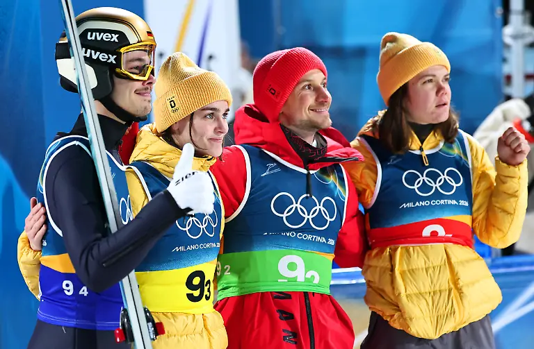 Olympia-Olympische-Winterspiele-Mailand-Cortina-2026-Ski-nordisch-Skispringen-Team-Mixed-Durchgang-2-Philipp-Raimund-l-Deutschland-reagiert-nach-seinem-Sprung-neben-den-Teamkollegen-Selina-Freitag-2-v-l-Felix-Hoffmann-2-v-r-und-Agnes-Reisch-alle-Deutschland
