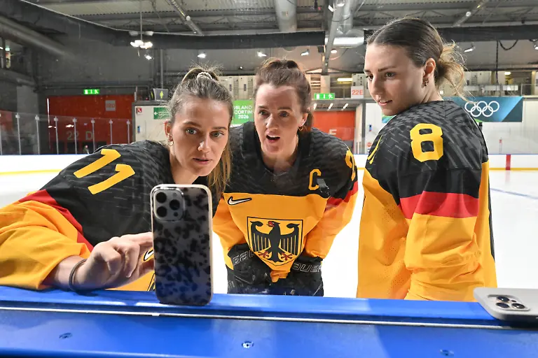 Olympia-Olympische-Winterspiele-Mailand-Cortina-2026-Eishockey-Frauen-Training-Deutschland-Die-deutschen-Spielerinnen-l-r-Nicola-Hadraschek-Eisenschmid-Daria-Gleissner-und-Ronja-Hark-schauen-auf-ein-Smartphone