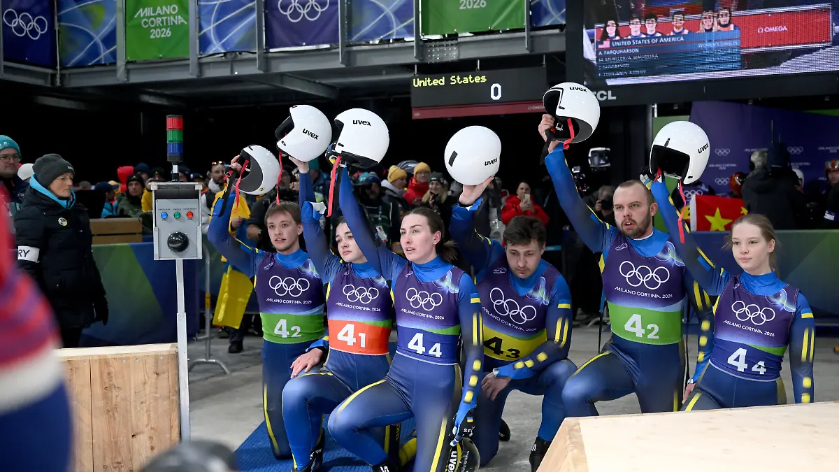 Olympia-Olympische-Winterspiele-Mailand-Cortina-2026-Rodeln-Staffel-Mixed-im-Cortina-Sliding-Centre-das-Team-der-Ukraine-kniet-am-Boden-und-hebt-im-Zielbereich-gemeinsam-die-Helme-nach-oben