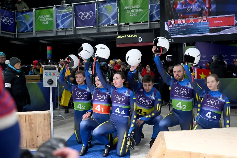 Olympia-Olympische-Winterspiele-Mailand-Cortina-2026-Rodeln-Staffel-Mixed-im-Cortina-Sliding-Centre-das-Team-der-Ukraine-kniet-am-Boden-und-hebt-im-Zielbereich-gemeinsam-die-Helme-nach-oben