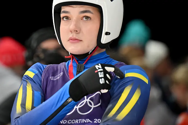 Olympia-Olympische-Winterspiele-Mailand-Cortina-2026-Rodeln-Staffel-Mixed-im-Cortina-Sliding-Centre-Julianna-Tunyzka-Ukraine-zeigt-im-Zielbereich-auf-die-Fahne-der-Ukraine-auf-ihrer-Schulter