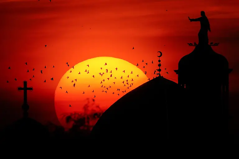 MOSUL-IRAQ-NOVEMBER-17-A-view-of-the-red-hues-that-appear-in-the-sky-during-sunset-creates-a-scene-framing-the-minaret-of-Imam-Muhsin-Mosque-alongside-the-Chaldean-Al-Tahira-Church-in-Mosul-Iraq-on-November-17-2025