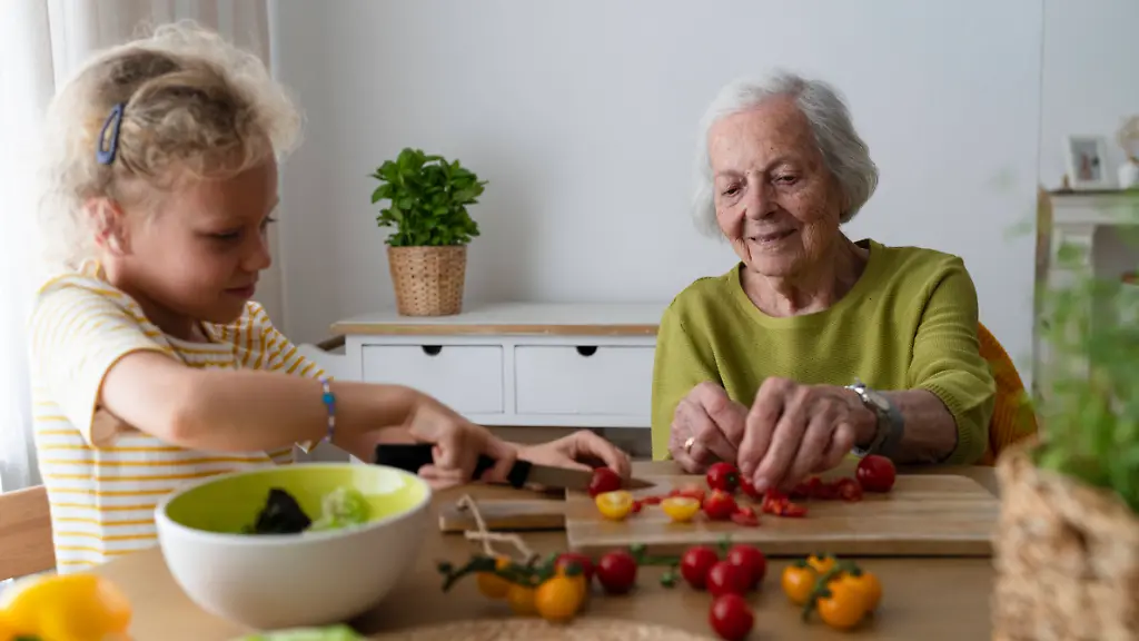 Smiling-grandmother-and-granddaughter-cutting-vegetables-on-table-model-released-Symbolfoto-property-released-SVKF01497