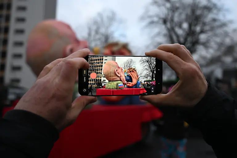 Ein-Mann-fotografiert-einen-Mottowagen-mit-Putin-und-Trump-die-versuchen-Europa-zu-fressen-mit-seinem-Handy-Der-Rosenmontag-am-Rhein-ist-der-Hoehepunkt-der-rheinischen-Karnevalssaison-mit-den-traditionellen-Umzuegen-unter-anderem-in-Koeln-Duesseldorf-und-Mainz