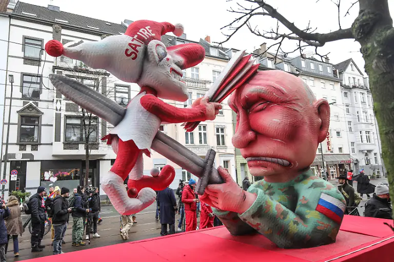 Mottowagen-des-Duesseldorfer-Bildhauers-Jacques-Tilly-am-Montag-16-02-2026-auf-dem-Duesseldorfer-Rosenmontagszug-Foto-Der-russische-Praesident-Wladimir-Putin-spiesst-den-Hoppeditz-mit-einem-Schwert-auf-Die-Duesseldorfer-Karnevalsfigur-wiederum-schlaegt-dem-in-Militaeruniform-gekleideten-Putin-mit-einer-Narrenpritsche-auf-den-Kopf-In-Moskau-laeuft-aktuell-ein-Prozess-gegen-den-Wagenbauer-Tilly-wegen-Verunglimpfung-der-russischen-Staatsorgane-Tilly-nimmt-nicht-an-dem-Verfahren-in-Russland-teil-Siehe-epd-Meldung-vom-16-02