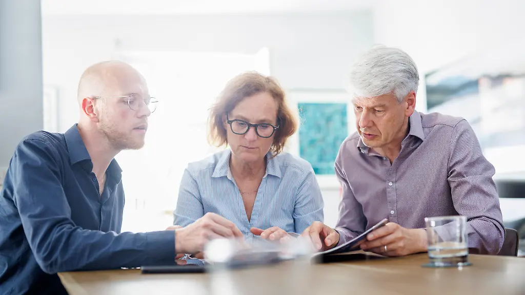 Symbolfoto-zum-Thema-Beratung-Eine-aeltere-Frau-und-ein-aelterer-Mann-sitzen-zu-Hause-zusammen-an-einem-Tisch-und-werden-von-einem-jungen-Mann-beraten-Berlin-13-08-2024