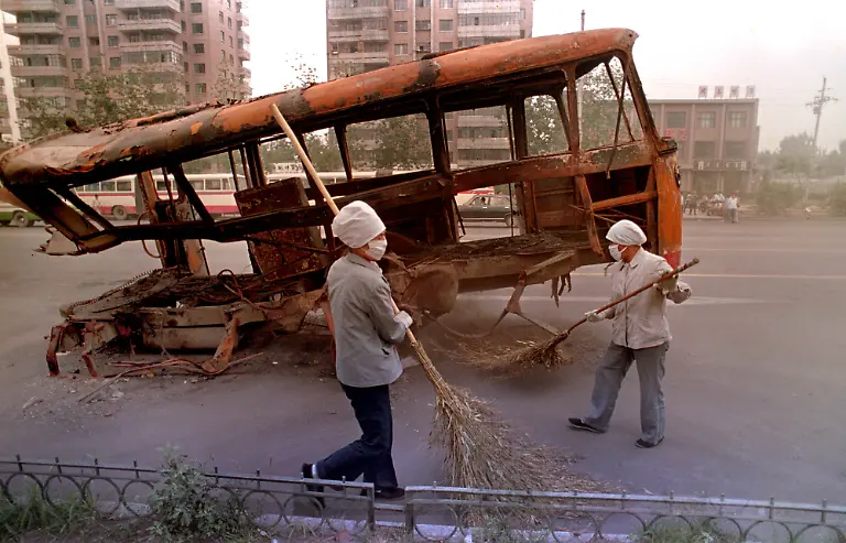 Street-sweepers-clean-around-a-burned-out-city-bus-on-Chang-an-Boulevard-in-Beijing-June-12-1989-The-bus-was-burned-in-the-anti-government-melee-when-it-was-placed-by-demonstrators-as-a-barricade-against-advancing-troops-a-week-earlier