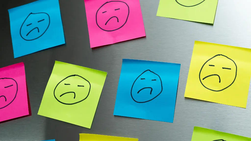 Bunte-Post-its-mit-traurigen-Gesichtern-symbolisieren-Unzufriedenheit-im-Job-und-die-Belastungen-im-Arbeitsalltag