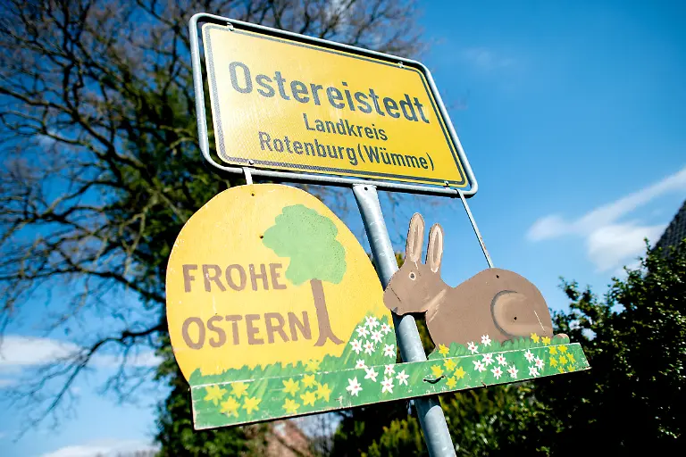 Ein-Schild-mit-der-Aufschrift-Frohe-Ostern-haengt-unter-dem-Ortsschild-am-Ortseingang-von-Ostereistedt-Eine-Rekordzahl-von-etwa-59-000-Briefen-ist-in-diesem-Jahr-beim-Osterpostamt-in-Ostereistedt-angekommen-Die-Briefe-werden-noch-bis-kommende-Woche-von-freiwilligen-Helfern-beantwortet