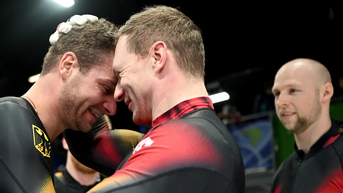 Olympia-Olympische-Winterspiele-Mailand-Cortina-2026-Bob-Viererbob-Maenner-Durchgang-4-im-Cortina-Sliding-Centre-Johannes-Lochner-Pilot-l-und-Francesco-Friedrich-Pilot-beide-Deutschland-jubeln-ueber-die-Gold-und-Silbermedaille-Dahinter-steht-Friedrichs-Anschieber-Alexander-Schueller-r