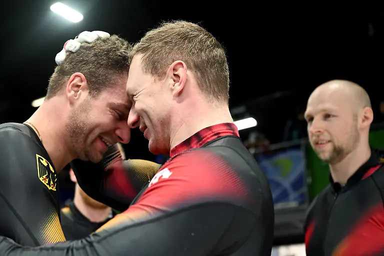 Olympia-Olympische-Winterspiele-Mailand-Cortina-2026-Bob-Viererbob-Maenner-Durchgang-4-im-Cortina-Sliding-Centre-Johannes-Lochner-Pilot-l-und-Francesco-Friedrich-Pilot-beide-Deutschland-jubeln-ueber-die-Gold-und-Silbermedaille-Dahinter-steht-Friedrichs-Anschieber-Alexander-Schueller-r