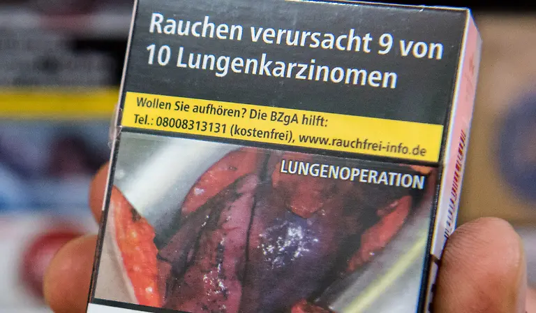 ARCHIV-ILLUSTRATION-Ein-Mann-haelt-am-26-06-2016-in-Hamburg-in-einem-Kiosk-eine-Zigarettenschachtel-auf-der-ein-Schockfoto-einer-Lungenoperation-und-der-Warnhinweis-Rauchen-verursacht-9-von-10-Lungenkarzinomen-aufgedruckt-sind-zu-dpa-Letzter-Abverkauf-Schockbilder-nun-auf-allen-Tabakschachteln-vom-18-05