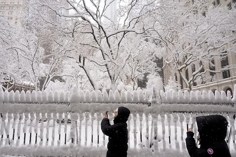 Pedestrians-stop-to-make-photos-of-Trinity-Church-graveyard-in-lower-Manhattan-during-a-snow-storm-Monday-Feb-23-2026-in-New-York