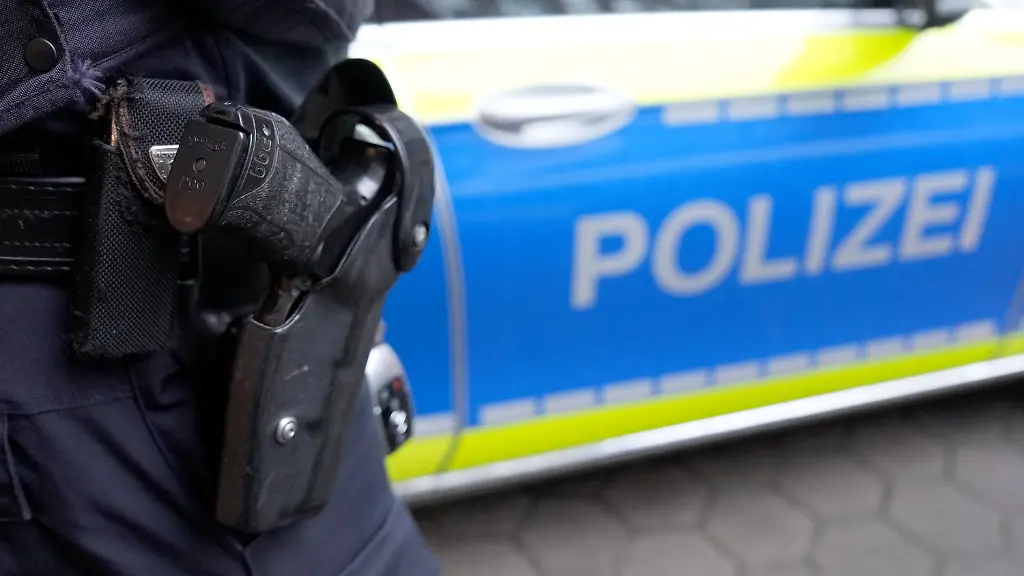 ARCHIV-15-03-2024-Hamburg-Ein-Polizist-steht-vor-einem-Einsatzfahrzeug-der-Polizei