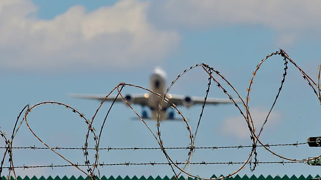 Symbolbild-Abschiebeflug-Ein-startendes-Flugzeug-hinter-einem-Stacheldrahtzaun