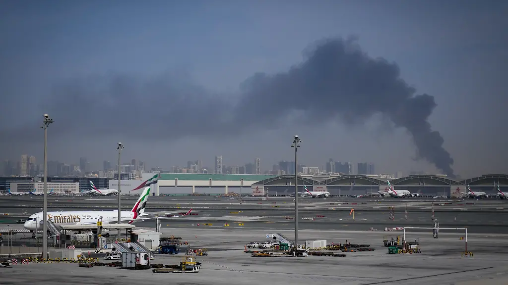 Eine-Rauchwolke-verursacht-durch-einen-iranischen-Angriff-ist-im-Hintergrund-zu-sehen-waehrend-Flugzeuge-der-Emirates-nach-der-Schliessung-des-Flughafens-auf-dem-Dubai-International-Airport-geparkt-sind