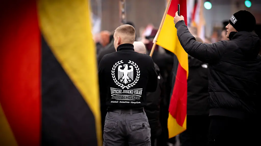 DEU-Deutschland-Germany-Berlin-29-11-2025-Demonstrant-mit-Shirt-Symbol-Adler-und-Logo-Deutsche-Jugend-Voran-Division-Senftenberg-Aktivistisch-Heimattreu-Kampfbereit-bei-dem-Marsch-Kundgebung-und-Demonstration-der-rechtsextremen-Partei-Die-Heimat-ehemals-NPD-unter-dem-Motto-Betrueger-und-Kriminelle-Auslaender-raus-und-Heimatschuetzer-in-Berlin-Deutschland-Neben-Mitgliedern-der-Heimat-und-der-Jugendorganisation-Junge-Nationalisten-JN-fanden-sich-auch-Mitglieder-Deutsche-Jugend-Voran-DJV-und-der-sog-Jaegergruppe-Jaegergruppe-Ein-breites-Buendnis-von-der-antifaschistischen-Aktion-antifa-bis-zu-Omas-gegen-rechts-konnte-mit-einer-Blockade-die-eigentliche-Demo-verhindern-en-Demonstrator-wearing-a-shirt-with-the-eagle-symbol-and-the-Logo-German-Youth-Forward-Division-Senftenberg-activist-patriotic-ready-for-battle-at-the-march-and-demonstration-of-the-far-right-party-Die-Heimat-formerly-NPD-under-the-motto-Cheaters-and-Criminals-Foreigners-Out-and-Homeland-Protectors-in-Berlin-Germany-Besides-members-of-the-Heimat-youth-organization-Young-Nationalists-Junge-Nationalisten-JN-members-of-the-Deutsche-Jugend-Voran-German-Youth-Forward-DJV-and-the-so-called-Hunter-Group-Jaegergruppe-were-also-present