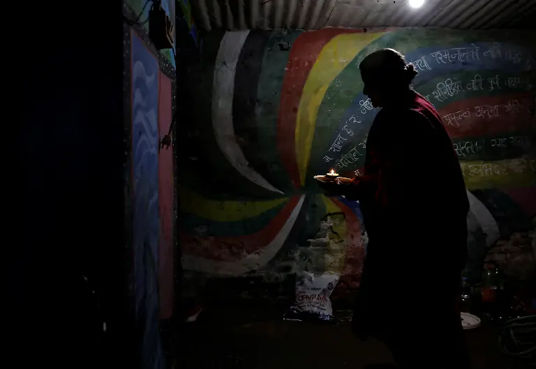 Lata-Maya-Maharjan-75-mother-of-Binod-Maharjan-34-who-was-shot-dead-during-youth-led-protests-that-toppled-Nepal-s-prime-minister-and-prompted-elections-set-for-March-5-2026-holds-an-oil-lamp-as-she-walks-past-paintings-made-by-Binod-that-cover-the-wall-of-her-house-returning-from-a-temple-after-offering-her-daily-prayers-in-Lalitpur-Nepal-February-21-2026-After-feeding-pigeons-on-the-terrace-like-he-did-most-mornings-Binod-abruptly-left-home-on-September-8-leaving-his-breakfast-of-rice-and-lentils-The-family-only-discovered-he-had-joined-the-swelling-protests-after-Binod-s-elder-brother-received-a-phone-call-from-one-of-his-sibling-s-childhood-friends-and-rushed-to-Kathmandu-s-Everest-Hospital-My-son-said-he-would-return-home-and-eat-the-meal-he-had-left-behind-said-Lata-Maya-He-never-came-back-REUTERS-Navesh-Chitrakar-SEARCH-CHITRAKAR-NEPAL-PROTESTER-FAMILIES-FOR-THIS-STORY-SEARCH-WIDER-IMAGE-FOR-ALL-STORIES