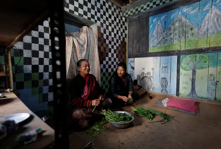 Lata-Maya-Maharjan-75-mother-of-Binod-Maharjan-34-who-was-shot-dead-during-youth-led-protests-that-toppled-Nepal-s-prime-minister-and-prompted-elections-set-for-March-5-2026-prepares-leafy-greens-with-her-daughter-Bindu-Maharjan-as-they-sit-next-to-paintings-made-by-Binod-that-cover-the-wall-of-her-house-in-Lalitpur-Nepal-February-21-2026-After-feeding-pigeons-on-the-terrace-like-he-did-most-mornings-Binod-abruptly-left-home-on-September-8-leaving-his-breakfast-of-rice-and-lentils-The-family-only-discovered-he-had-joined-the-swelling-protests-after-Binod-s-elder-brother-received-a-phone-call-from-one-of-his-sibling-s-childhood-friends-and-rushed-to-Kathmandu-s-Everest-Hospital-My-son-said-he-would-return-home-and-eat-the-meal-he-had-left-behind-said-Lata-Maya-He-never-came-back-REUTERS-Navesh-Chitrakar-SEARCH-CHITRAKAR-NEPAL-PROTESTER-FAMILIES-FOR-THIS-STORY-SEARCH-WIDER-IMAGE-FOR-ALL-STORIES