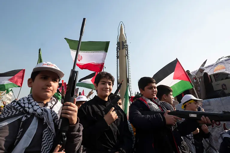 Iranian-schoolboys-as-members-of-the-Basij-paramilitary-force-under-the-command-of-the-Islamic-Revolutionary-Guard-Corps-IRGC-carry-pistols-and-rifles-while-walking-under-an-Iranian-made-surface-to-surface-ballistic-missile-during-a-military-rally-in-downtown-Tehran-Iran-on-January-10-2025-The-Basij-Resistance-Force-commonly-known-as-the-Basij-is-established-on-December-26-1979-by-the-order-of-Ayatollah-Ruhollah-Khomeini-According-to-Article-13-of-the-Islamic-Revolutionary-Guard-Corps-IRGC-Employment-Regulations-a-Basiji-is-a-volunteer-who-joins-the-IRGC-s-20-million-strong-force-The-Basij-plays-a-significant-role-in-Iran-s-history-particularly-during-the-Iran-Iraq-War-and-continues-to-be-a-prominent-paramilitary-force-under-the-IRGC