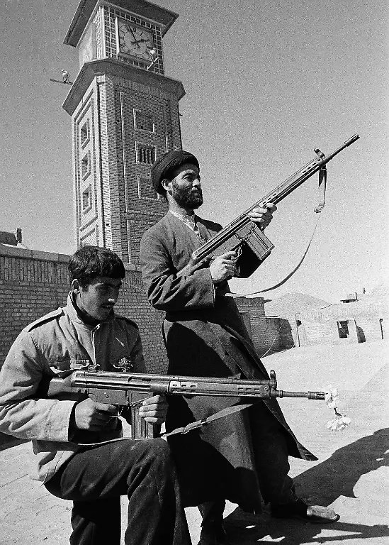 A-Muslim-priest-right-and-a-revolutionary-guard-with-a-white-carnation-in-his-rifle-barrel-keep-a-vigil-watch-on-a-roof-on-the-town-square-in-Qom-Iran-where-the-Ayatollah-Khomeini-addressed-the-crowd-March-1-1979-The-Ayatollah-was-arrested-in-Qom-18-years-ago-by-the-Shah-s-police-and-lived-in-exile-until-Feb-1-1979-when-returned-to-Iran