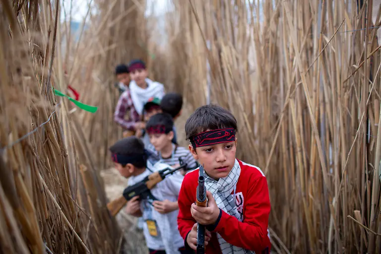 A-group-of-children-aged-seven-to-fourteen-carry-plastic-AK-47-rifles-and-take-part-in-a-military-performance-near-the-Iranian-border-at-Shalamcheh-with-Iraq-918-km-570-miles-south-of-Tehran-Iran-on-March-24-2014-Children-aged-seven-to-fourteen-in-an-area-near-the-Shalamcheh-border-in-southern-Iran-with-Iraq-reenact-the-military-operation-for-the-liberation-of-Khorramshahr-which-the-Iraqi-army-occupied-at-the-outset-of-the-IraqaIran-war-in-1980-A-group-of-Basij-military-personnel-under-the-command-of-the-Islamic-Revolutionary-Guard-Corps-IRGC-plans-and-carries-out-the-performance
