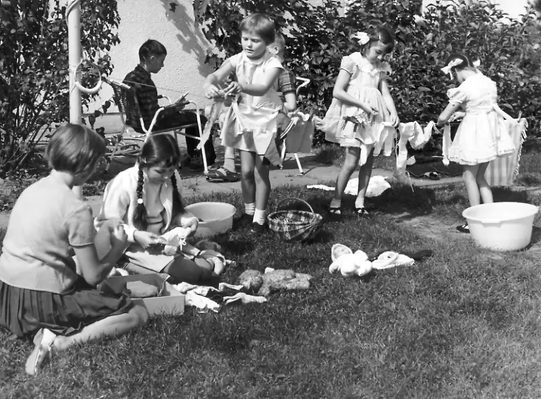 Eine-Gruppe-Maedchen-in-ihren-Sonntagskleidchen-ueben-mit-dem-Waschen-und-Trocknen-der-Kleidung-ihrer-Puppen-in-einem-Garten-schon-mal-das-Hausfrauen-Dasein-Aufnahme-vom-September-1965
