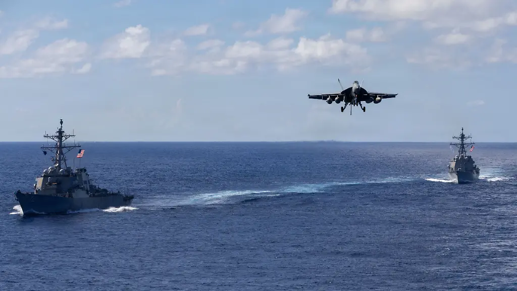 Auf-diesem-von-der-Pressestelle-des-Pentagons-zur-Verfuegung-gestellten-Bild-fahren-die-Lenkwaffenzerstoerer-der-Arleigh-Burke-Klasse-USS-Mahan-l-DDG-72-und-USS-Bainbridge-DDG-96-in-Formation-waehrend-ein-F-A-18-Super-Hornet-des-Carrier-Air-Wing-Eight-zur-Landung-auf-dem-Flugzeugtraeger-USS-Gerald-R-Ford-CVN-78-ansetzt