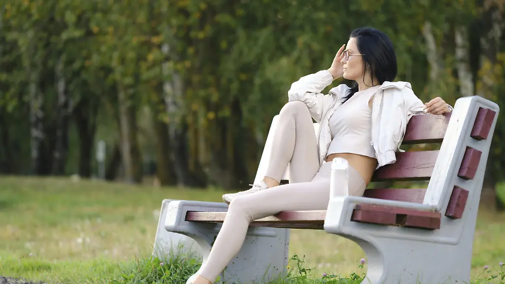 Eine-Frau-sitzt-auf-einer-Parkbank-bekleidet-mit-leichter-Sportkleidung-und-geniesst-den-warmen-Tag
