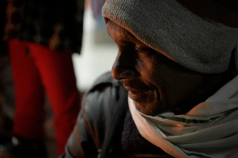 Firelight-illuminates-the-face-of-security-guard-Pannelal-Rajak-78-as-he-sits-with-a-group-of-women-from-the-Shiv-Shakti-Mahila-Gram-Sangathan-self-help-group-at-the-start-of-his-night-shift-at-Kenapara-Eco-Park-which-was-developed-from-a-closed-open-cast-coal-mine-pit-into-a-small-tourist-hub-in-Surajpur-India-November-16-2025-Decades-ago-Rajak-gave-up-his-land-for-the-Bishrampur-open-cast-coal-mine-in-exchange-for-money-and-a-job-in-the-mine-he-believed-would-follow-but-he-never-got-the-job-Today-he-guards-the-same-mine-At-least-I-am-earning-something-here-now-he-says-REUTERS-Avijit-Ghosh-SEARCH-INDIA-GHOSH-COAL-FOR-THIS-STORY-SEARCH-WIDER-IMAGE-FOR-ALL-STORIES