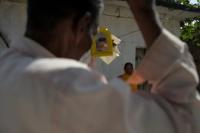 Pannelal-Rajak-78-who-is-a-security-guard-at-Kenapara-Eco-Park-which-was-developed-from-a-closed-open-cast-coal-mine-pit-into-a-small-tourist-hub-fixes-his-hair-after-returning-from-a-night-shift-as-his-wife-stands-in-front-of-him-in-their-courtyard-in-Surajpur-India-November-16-2025-Decades-ago-Rajak-gave-up-his-land-for-the-Bishrampur-open-cast-coal-mine-in-exchange-for-money-and-a-job-in-the-mine-he-believed-would-follow-but-he-never-got-the-job-Today-he-guards-the-same-mine-At-least-I-am-earning-something-here-now-he-says-REUTERS-Avijit-Ghosh-SEARCH-INDIA-GHOSH-COAL-FOR-THIS-STORY-SEARCH-WIDER-IMAGE-FOR-ALL-STORIES