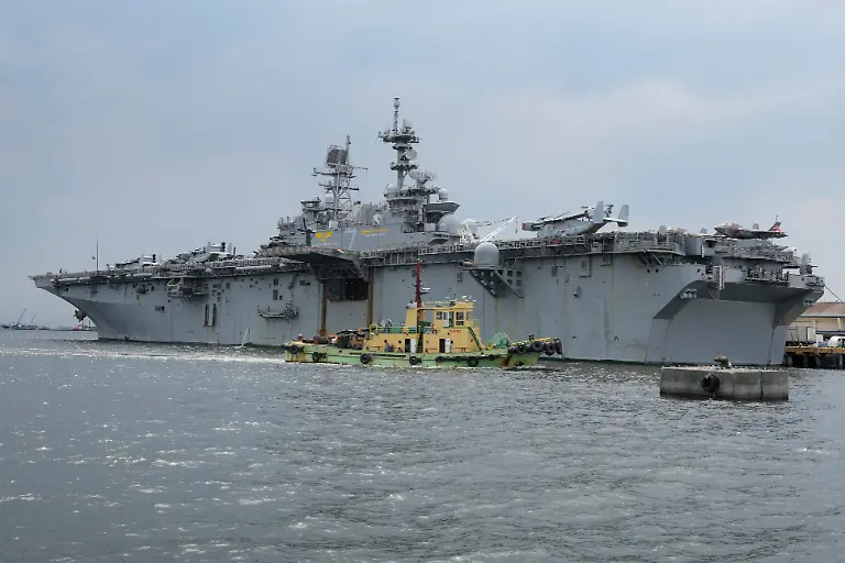 A-tugboat-passes-by-a-U-S-Navy-USS-Tripoli-LHA-7-amphibious-assault-ship-during-a-port-call-in-Manila-Philippines-Tuesday-Sept-27-2022