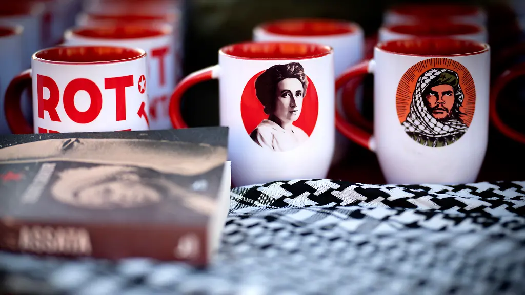 DEU-Deutschland-Germany-Berlin-11-01-2026-Stand-mit-Verkauf-von-Tassen-mit-Motiv-Rot-Front-Bild-von-Rosa-Luxemburg-und-Ernesto-Che-Guevara-mit-Palaestinensertuch-auch-Kufiya-genannt-an-der-Gedenkstaette-der-Sozialisten-als-Souvenir-bei-dem-linken-Gedenken-bei-der-Gedenkstaette-der-Sozialisten-in-Berlin-Friedrichsfelde-anlaesslich-der-Luxemburg-Liebknecht-Gedenkveranstaltung-in-Berlin-Deutschland-Der-Gedenktag-erinnert-an-den-Jahrestag-der-Ermordung-der-Kommunisten-Rosa-Luxemburg-und-Karl-Liebknecht-am-15-Januar-1919-Seit-dem-Ende-der-DDR-hat-die-Veranstaltung-unter-der-Teilnahme-der-Linkspartei-Die-Linke-eine-neue-Beliebtheit-hauptsaechlich-unter-Ostdeutschen-und-zunehmend-jungen-Menschen-erfahren-en-Stall-selling-mugs-with-a-red-front-design-an-image-of-Rosa-Luxemburg-and-Ernesto-Che-Guevara-wearing-a-kufiya-Palestinian-scarf-during-the-left-wing-commemoration-at-the-Memorial-to-the-Socialists-in-Berlin-Friedrichsfelde-on-the-occasion-of-the-Luxemburg-Liebknecht-memorial-event-in-Berlin-Germany