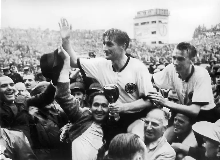 ARCHIV-Der-deutsche-Stuermer-und-Kapitaen-Fritz-Walter-M-oben-und-sein-Lauterer-Teamgefaehrte-Horst-Eckel-r-werden-nach-dem-Triumph-im-Fussball-WM-Finale-im-Berner-Wankdorfstadion-von-begeisterten-Anhaengern-vom-Spielfeld-getragen-Archivfoto-vom-04-07-1954-Fritz-Walter-haelt-den-Jules-Rimet-Pokal-in-der-Hand-den-er-mit-seiner-Mannschaft-gewinnt-Die-deutsche-Fussballnationalmannschaft-besiegt-Ungarn-vor-56-000-Zuschauern-darunter-5000-deutschen-mit-3-2-und-sichert-sich-erstmals-den-Weltmeistertitel-Foto-dpa-zu-dpa-Meldung-Das-Wunder-von-Bern-Tor-Rekord-und-Doping-Verdacht-vom-03-06