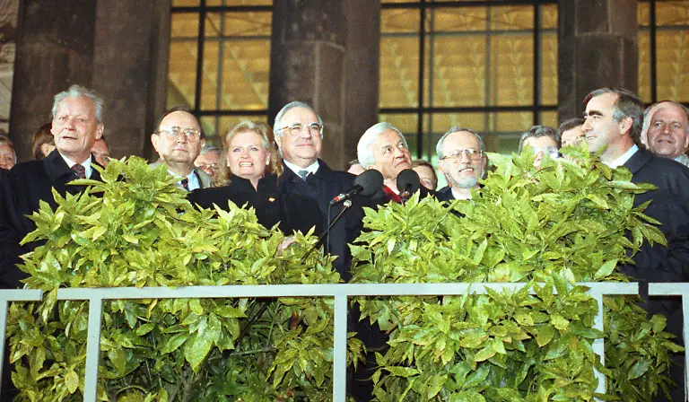 Die-Deutschen-sind-wieder-vereint-Bei-der-Berliner-Feier-am-03-10-1990-winken-von-der-Freitreppe-des-Reichstagsgebaeude-l-r-Alt-Bundeskanzler-Willy-Brandt-SPD-Bundesaussenminister-Hans-Dietrich-Genscher-FDP-Hannelore-Kohl-Bundeskanzler-Helmut-Kohl-CDU-und-Bundespraesident-Richard-von-Weizsaecker-daneben-Lothar-de-Maiziere-der-letzte-DDR-Ministerpraesident-und-links-im-Profil-Theo-Waigel-CSU-Die-Deutschen-sind-45-Jahre-nach-dem-Ende-des-2-Weltkrieges-mit-dem-3-Oktober-1990-wieder-in-einem-souveraenen-Staat-vereint-Die-DDR-ist-der-Bundesrepublik-beigetreten-und-existiert-nicht-mehr-Der-Untergang-des-SED-Regimes-hatte-sich-in-einem-rasanten-Tempo-vollzogen-Am-9-11-1989-oeffnete-die-DDR-endgueltig-ihre-Grenzen