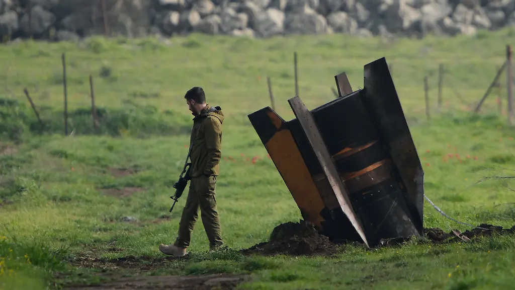 Ein-israelischer-Soldat-steht-neben-einem-Fragment-einer-vom-Iran-abgefeuerten-und-vom-israelischen-Luftabwehrsystem-abgefangenen-Rakete-auf-einem-offenen-Feld-in-den-israelisch-kontrollierten-Golanhoehen