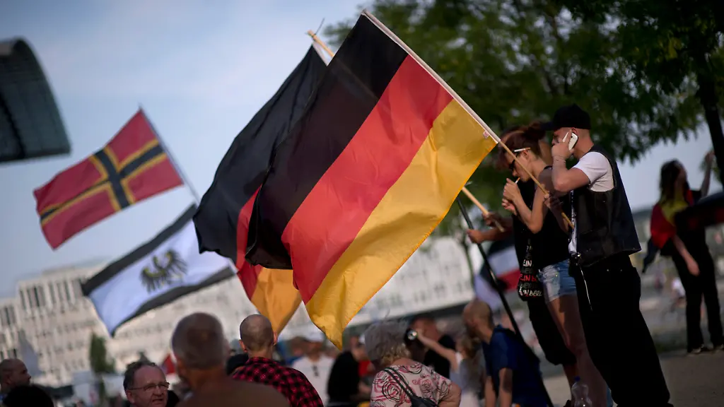 DEU-Deutschland-Germany-Berlin-10-08-2015-Demonstranten-mit-Fahnen-Kreuz-Fahne-in-Schwarz-Rot-Gold-nach-Josef-Wirmer-auf-der-Demonstration-von-Pegida-Patriotische-Europaeer-Gegen-die-Islamisierung-des-Abendlandes-oder-Baergida-bzw-Bergida-am-Haupzbahnhof-im-Regierungsviertel-in-Berlin-Die-sogenannte-Buergerbewegung-Pegida-ist-eine-Gruppe-in-Dresden-die-eine-Islamisierung-Deutschlands-und-Europas-behauptet-und-ablehnt-Seit-Oktober-2014-gibt-es-woechentliche-Demonstrationen-gegen-eine-aus-ihrer-Sicht-verfehlte-europaeische-und-deutsche-Migrations-und-Asylpolitik-Aehnliche-Demonstrationen-finden-auch-in-einigen-anderen-deutschen-Staedten-statt-Sozialwissenschaftler-beurteilen-die-meisten-Teilnehmer-als-ueberwiegend-buergerlich-konservativ-teils-mit-auch-rechtspopulistischen-bis-rechtsextremen-Einstellungen-Supporters-and-Demonstrants-with-flags-at-a-rally-of-the-German-right-wing-populist-Pegida-movement-Patriotic-Europeans-Against-the-Islamisation-of-the-Occident-who-call-themselves-as-Baergida-or-Bergida-participate-at-a-demonstration-at-the-government-quarter-in-Berlin-Germany-Pegida-is-an-acronym-for-Patriotische-Europaeer-Gegen-die-Islamisierung-des-Abendlandes-or-Patriotic-Europeans-Against-the-Islamification-of-the-West-and-has-quickly-gained-local-mass-appeal-by-demanding-a-more-restrictive-policy-on-Germany-s-acceptance-of-foreign-refugees-and-asylum-seekers
