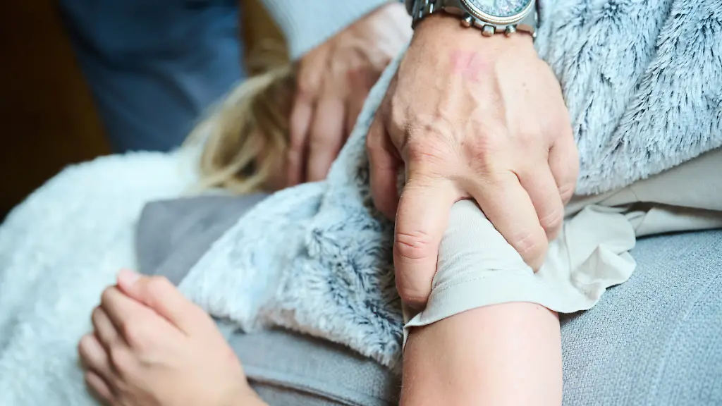 Eine-erwachsene-Person-greift-ein-Kind-fest-an-Arm-und-Kopf-waehrend-es-auf-einer-Couch-liegt