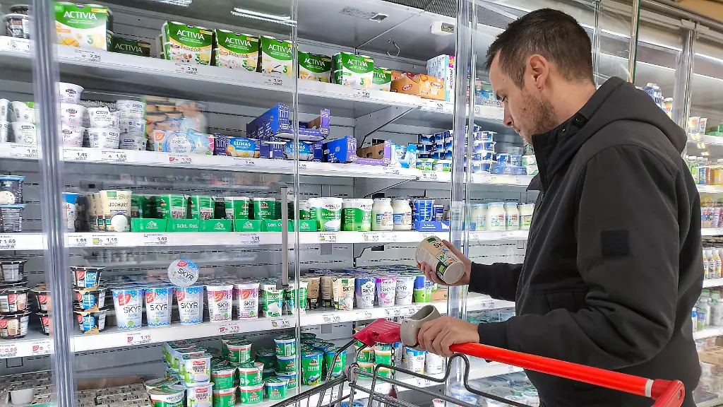 Ein-Kunde-prueft-im-Supermarkt-vor-dem-Kuehlregal-das-Etikett-eines-Milchprodukts-Sichtbar-sind-Verpackungen-und-Produkte-was-Themen-wie-Kennzeichnung-Naehrwertangaben-Verbraucherinformation-Auswahl-und-bewusste-Kaufentscheidungen-betont