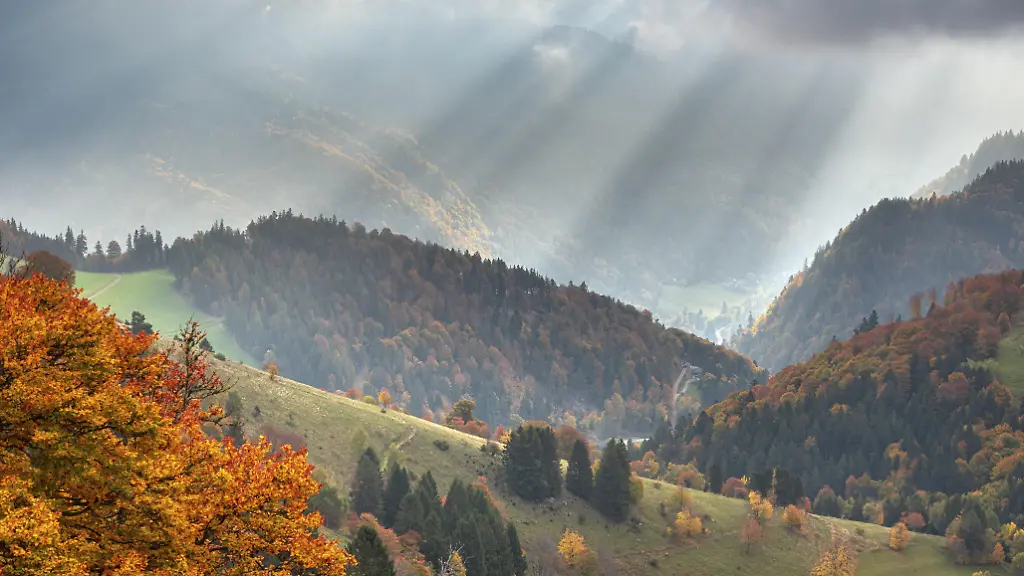 Ausblick-ueber-typische-Schwarzwaldlandschaft-mit-steilen-Wiesen-und-Waeldern-am-Schauinsland-Baeume-in-voller-Herbstfaerbung-Sonnenstrahlen-brechen-durch-die-Wolken-Schwarzwald-Baden-Wuerttemberg-Deutschland
