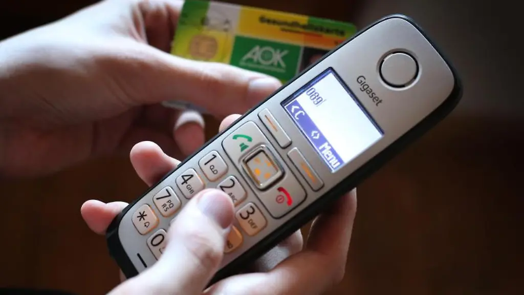 Ein-Mann-haelt-der-AOK-in-der-Hand-waehrend-er-am-Telefon-eine-Nummer-waehlt