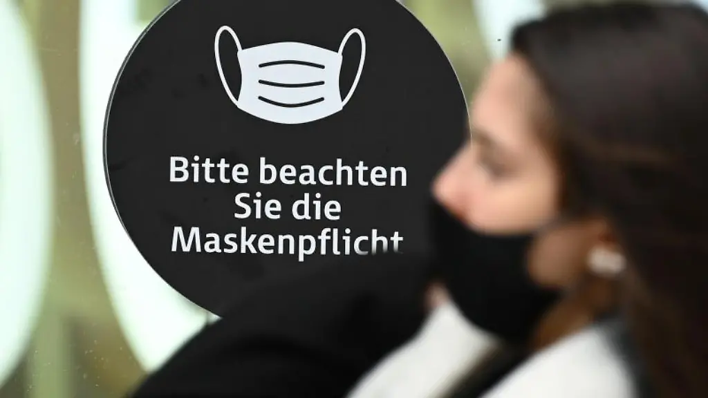 Eine-Frau-die-einen-Mund-Nasen-Schutz-traegt-an-einem-Hinweis-mit-der-Aufschrift-Bitte-beachten-Sie-die-Maskenpflicht-vorbei